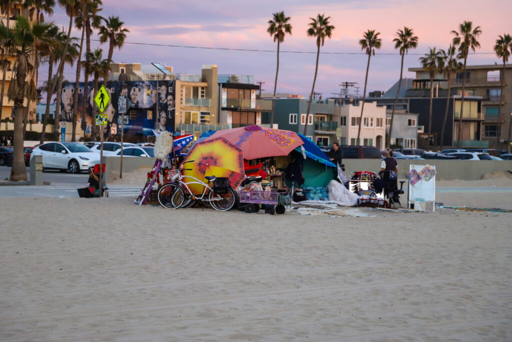 Homeless encampment with tents and scattered belongings at a California beach